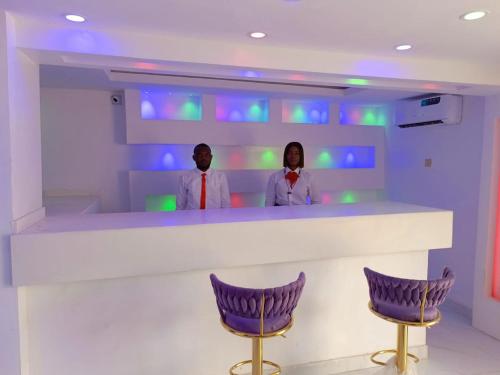 zwei Personen stehen an einer Bar mit lila Stühlen in der Unterkunft Global Signature Hotel and Resort in Ibadan