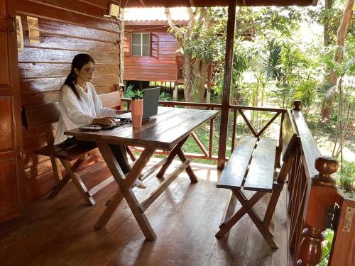 une femme assise à une table en bois sur une terrasse couverte dans l'établissement เชียงคานเรือนไม้ รีสอร์ท, à Amphoe Chiang Khan