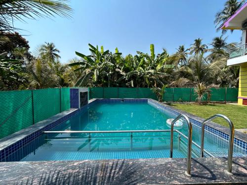 a swimming pool with a fence and palm trees at Anand Heritage Villa in Nagaon