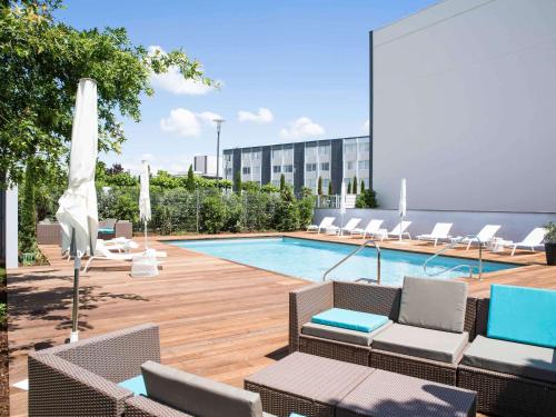 a swimming pool with lounge chairs and a building at Novotel Bordeaux Lac in Bordeaux