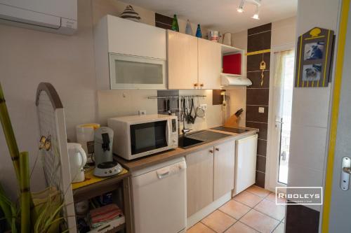 une cuisine avec des armoires blanches et un micro-ondes dans l'établissement Vias-plage - Maison climatisée à 450m de la mer, à Vias