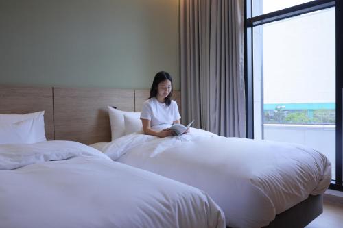 a woman sitting on a bed in a hotel room at From H Heritage Hotel in Mokpo