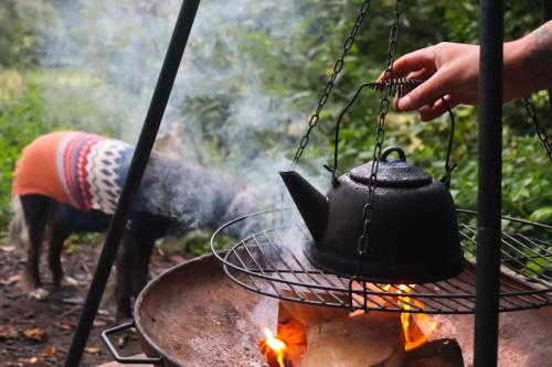 eine Person, die einen schwarzen Teekessel über einem Feuer hält in der Unterkunft Oku Wooden Pod, Newburgh Priory Estate in York