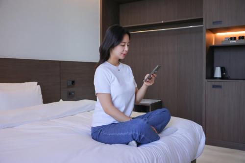 a woman sitting on a bed looking at her cell phone at From H Heritage Hotel in Mokpo