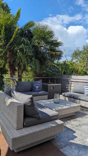 two wicker couches sitting on a patio with palm trees at Sonnendeck exklusives Haus in Meerbusch - Wellness Oase Whirlpool & Grill in Meerbusch