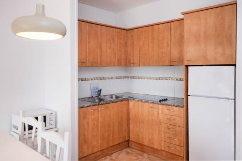cocina con armarios de madera y nevera blanca en Apartamentos Torrevella, en L'Estartit