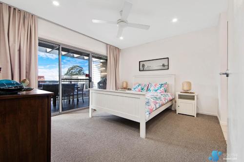 a white bedroom with a bed and a balcony at Batemans Bay Apartment in Batemans Bay