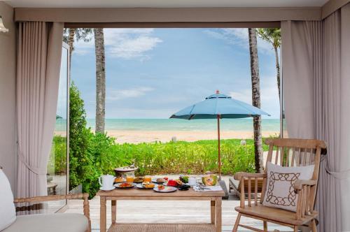 a room with a table and a view of the ocean at Devasom Khao Lak Beach Resort & Villas in Khao Lak