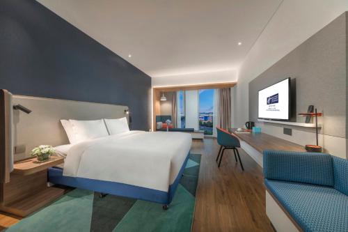 Holiday Inn Express Qingdao Chengyang Central by IHG في تشينغداو: غرفة نوم بها سرير ومكتب وتلفزيون