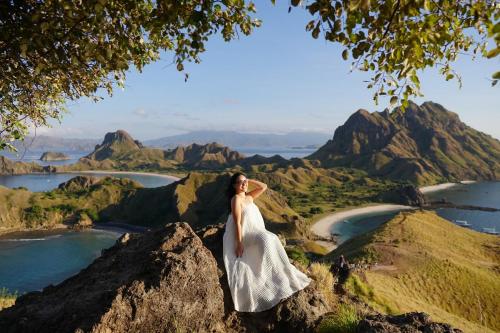 Una donna con un vestito bianco in piedi sulla cima di una montagna di DAV Travels a Labuan Bajo