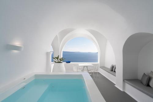 Habitación blanca con piscina y ventana abovedada en Katikies Villa Santorini - The Leading Hotels Of The World, en Oia