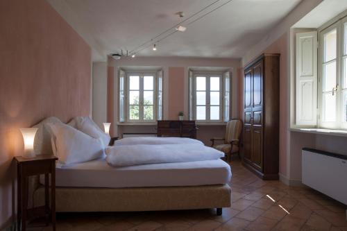 una camera da letto con letto, lenzuola bianche e finestre di Relais Villa Margherita a Oggebbio