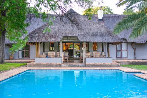 a house with a thatched roof and a swimming pool at Mziki Safari Lodge in Vaalkop Dam