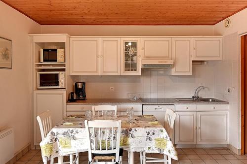 une cuisine avec une table avec des chaises et des armoires blanches dans l'établissement Les Chênes Rouges - Appt avec piscine partagée, à Gérardmer