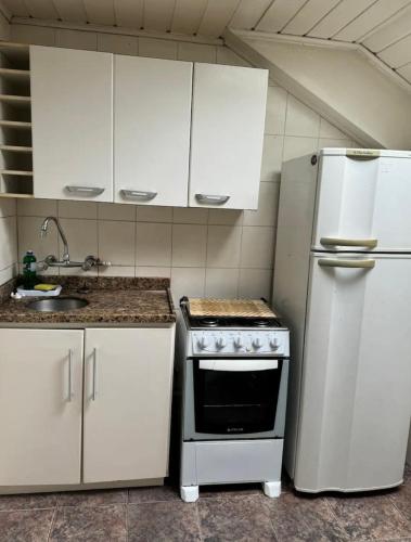 uma cozinha com armários brancos, um fogão e um frigorífico em Apartamento Aconchego Gramado em Gramado