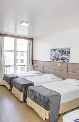 three beds in a room with a large window at Hotel Dan Inn Planalto São Paulo in Sao Paulo