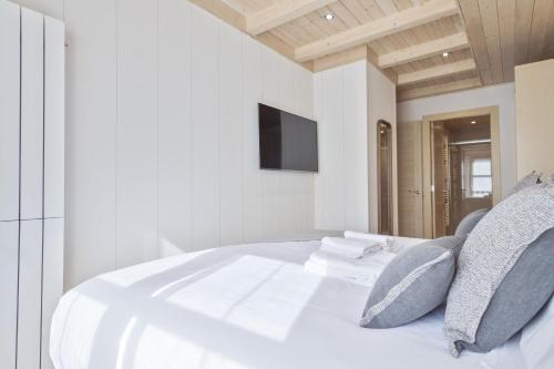 a white bed with pillows and a tv on the wall at Luderna - Apartamento Val de Ruda A38 de Sanèla in Baqueira-Beret