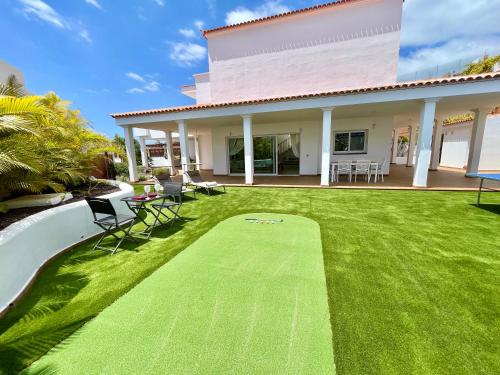 een tuin met een groen gazon met stoelen en een huis bij Beautiful Villa Amorio - Private Heated Pool with Sea Views & WIFI in Adeje