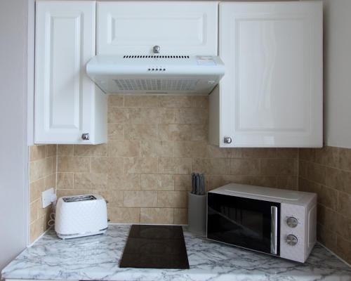 uma cozinha com armários brancos e um micro-ondas em 1 bedroom apartment - The Opal em Cheltenham