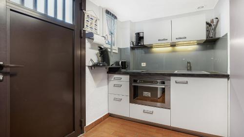 une cuisine avec des placards blancs et une porte noire dans l'établissement GREEN VILLAGE -7- Appt Lumineux 4 pers, au Cap d'Agde