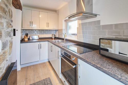 a kitchen with white cabinets and a sink and a stove at Host & Stay - Rose Cottage in Thropton