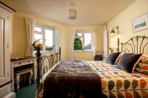 a bedroom with a bed and a desk and windows at Old Round House with hot tub in Padstow