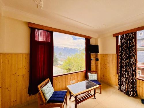 Cette chambre dispose d'une grande fenêtre et d'une table avec des chaises. dans l'établissement The Suraj lodge, Hadimba Road Manali, à Manali