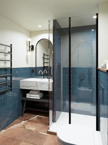W łazience znajduje się umywalka i prysznic z niebieskimi kafelkami. w obiekcie Hôtel Gabbie w Paryżu