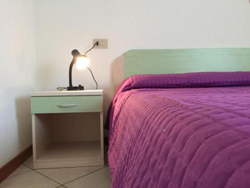 a bed with a purple blanket and a lamp on a night stand at Settimo cielo in Rosolina Mare