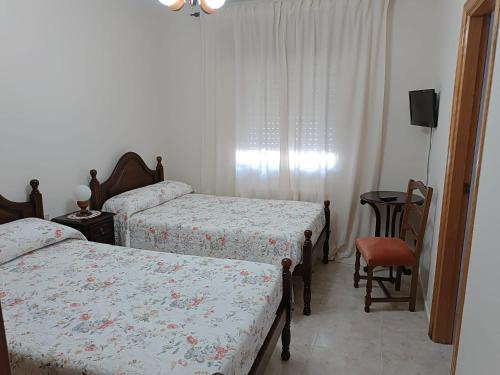 a bedroom with two beds and a table and a chair at PENSIÓN* AS VIÑAS in Puebla del Brollón