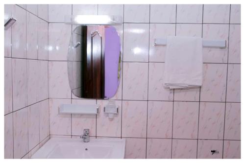 a white tiled bathroom with a mirror and a sink at Résidences K and D CAMOCO in Bafoussam