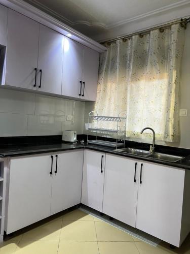cocina con armarios blancos, fregadero y ventana en CNJ’s Tranquil Haven en Kampala