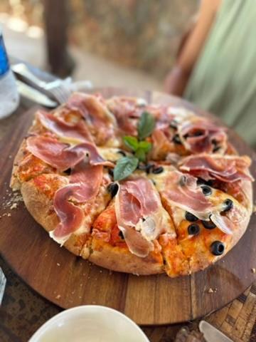 a pizza with ham and olives on a wooden cutting board at Kiwengwa Bungalow Boutique Resort in Kiwengwa