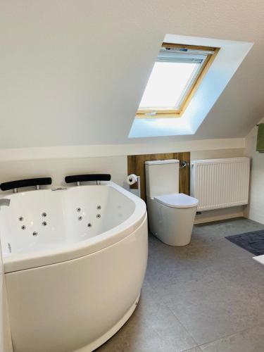 La salle de bains est pourvue d'une grande baignoire blanche et d'une lucarne. dans l'établissement Un air de campagne, à Châtenois