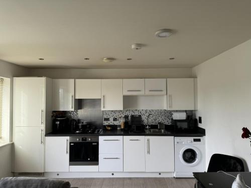 cocina con armarios blancos, lavadora y secadora en Inviting 2-Bed Apartment in Bushey, en Bushey