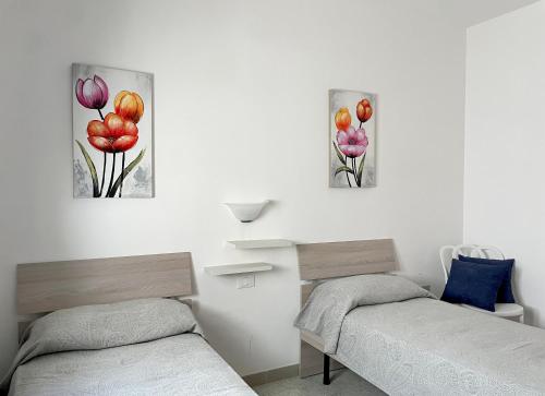 two beds in a room with three paintings on the wall at Casa Ermes - Piano terra indipendente fronte spiaggia, ampio spazio esterno attrezzato in Marina di Pescoluse
