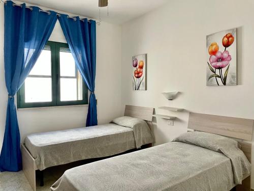 two beds in a room with blue curtains and a window at Casa Ermes - Piano terra indipendente fronte spiaggia, ampio spazio esterno attrezzato in Marina di Pescoluse