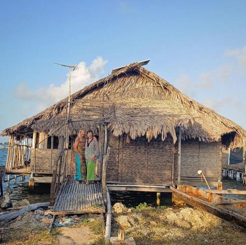 2 personnes debout en face d'une cabane au toit de chaume dans l'établissement Private Traditional Hut on the water with 2 rooms, à Wichubualá