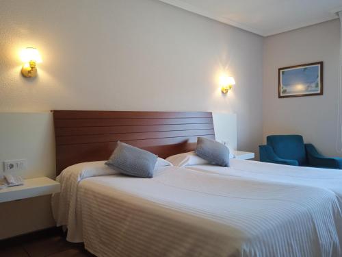 a hotel room with two beds and two blue chairs at Hotel Sablón in Llanes