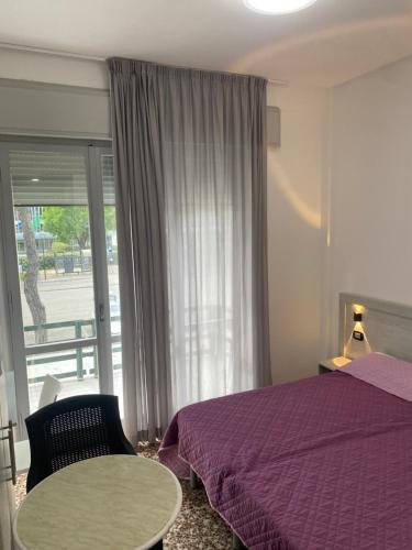 um quarto com uma cama roxa, uma mesa e uma janela em MDP Hotel em Cervia