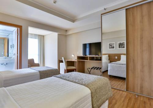 a hotel room with two beds and a mirror at Matiz Vilaboim Ribeirão Preto in Ribeirão Preto