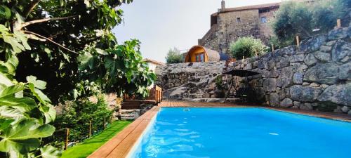 a swimming pool in front of a stone wall at Lagarto Pintado Casa n'Aldeia in Castelo Novo
