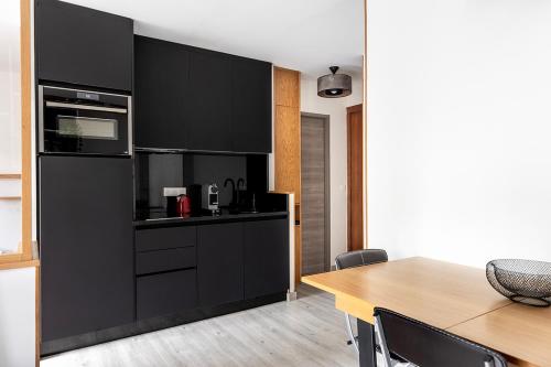 une cuisine avec des armoires noires et une table en bois dans l'établissement Studio avec balcon, proche de Paris tout équipé, à Asnières-sur-Seine