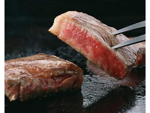 two pieces of meat cooking on a grill with tongs at Hotel Takimoto - Vacation STAY 43492v in Yamanouchi