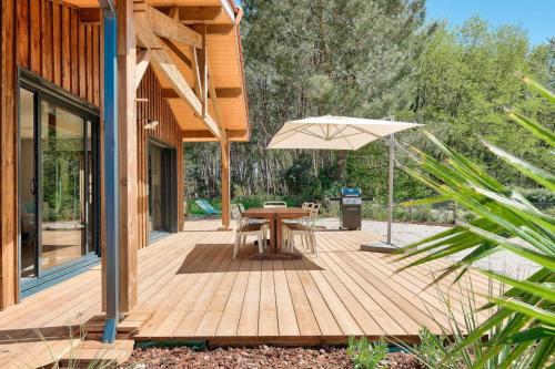 una terraza de madera con mesa y sombrilla en Peaceful house on the edge of a forest, en Sanguinet