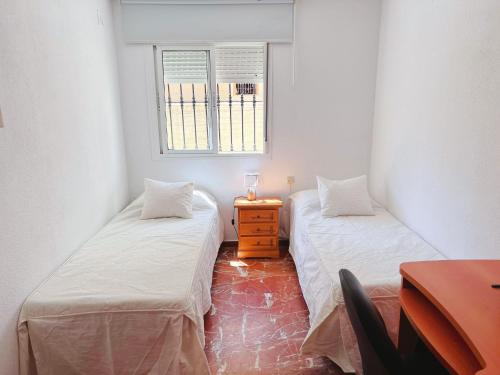 two beds in a room with a table and a window at Habitación compartido Huelva centro in Huelva