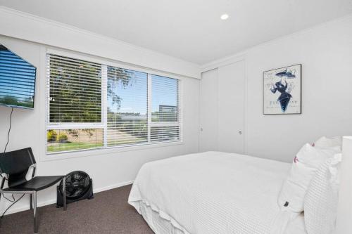 Un dormitorio blanco con una cama, una silla y una ventana. en Te Moenga Treasure - Acacia Bay, en Taupo