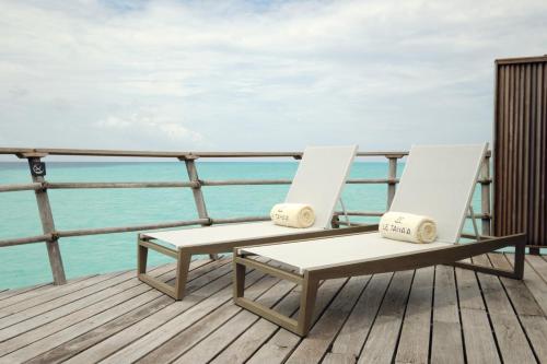 two white chairs sitting on a deck overlooking the ocean at Le Taha'a by Pearl Resorts in Motu Tautau