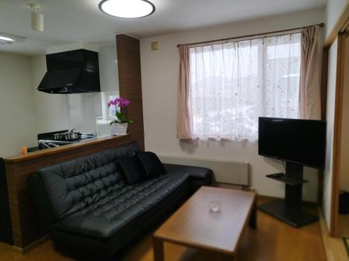 a living room with a black leather couch and a window at Guest House Nishimiyanosawa in Teine