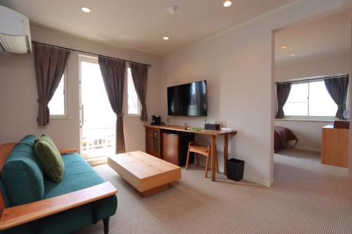 a living room with a couch and a desk with a television at Pension Angelica in Minami Aso